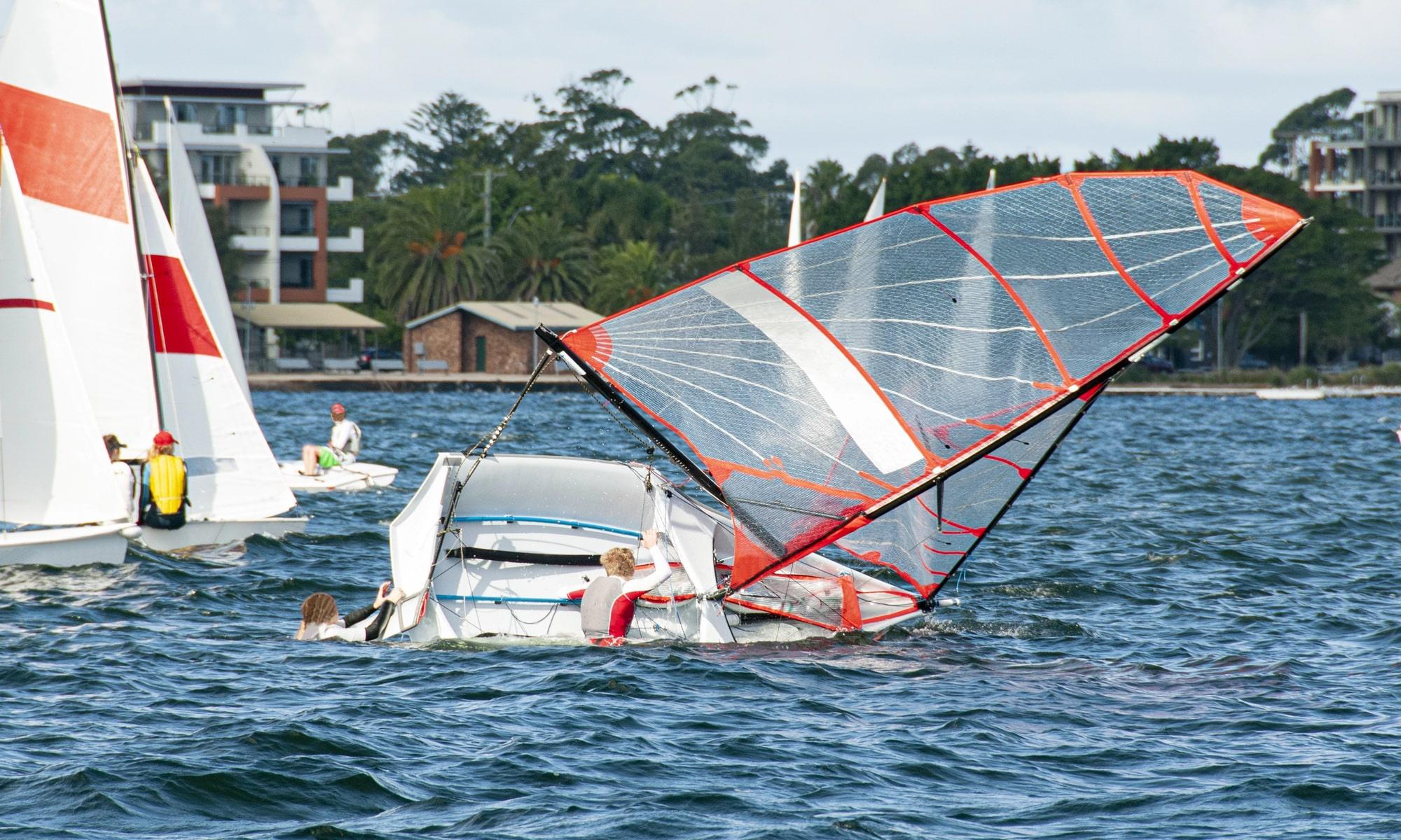 Capsized sailboat with occupants in the water after a boating accident on a coastal waterway